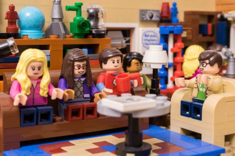 Szene aus der Serie "Big Bang Theory" aus Lego nachgestellt: Figuren sitzen in einem Wohnzimmer vor einem Couchtisch auf dem Sofa, im Hintergrund regale mit wissenschaftlichen Objekten