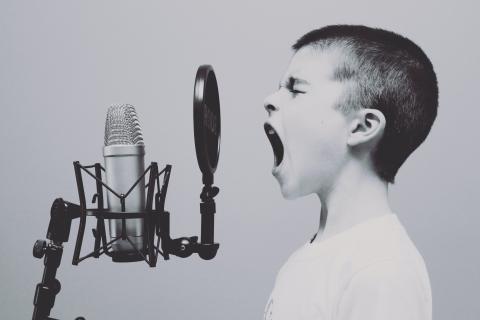 Schwarz-weiß Foto eines Kindes, das mit zusammengekniffenen Augen in ein Standmikrofon schreit