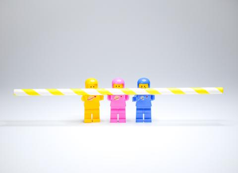 Drei Legofiguren im gelben, rosafarbenen und blauen Raumanzug halten einen gelb-weiß gekringelten Trinkhalm hoch